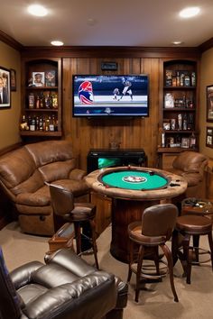 A cozy game room with a poker table, leather chairs, a TV displaying a football game, and shelves with memorabilia. Basement Board Game Room, Garage Makeover Man Cave, Man Cave Design Ideas, Man Cave Ideas Room, Small Man Cave Ideas, Man Cave Designs, Man Cave Inspiration, Small Man Cave, Cave Design