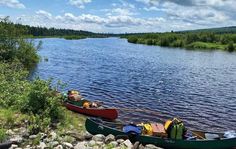 two canoes on the shore of a lake with trees in the background and rocks around them