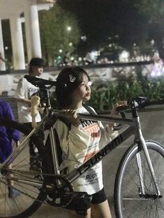 a woman carrying a bicycle on the back of her shoulder while standing in front of a building at night