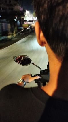 a man riding a motorcycle down a street at night with his helmet on the handlebars