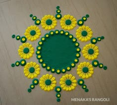 a green and yellow circular design on a wooden surface with circles in the center, surrounded by small yellow flowers