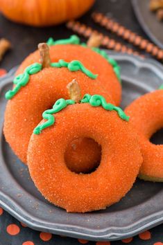 two pumpkin donuts on a plate with green frosting and sprinkles