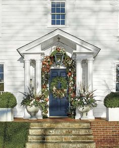 a blue front door with wreaths and potted plants on the steps in front of it