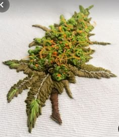 a close up of a green plant on a white table cloth with orange and yellow thread