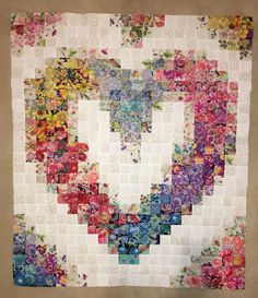 a heart shaped quilt with many different colors and shapes on the front, as well as flowers