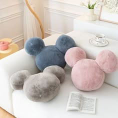 three mickey mouse pillows sitting on top of a white couch next to an open book