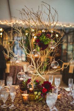 the centerpiece is decorated with branches and glass globes as well as flowers, greenery and candles