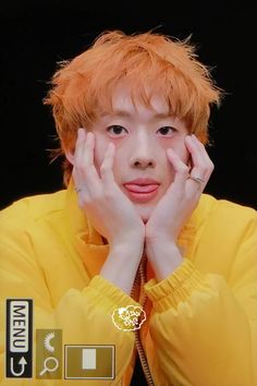 an orange haired man with his hands on his face and looking at the camera while wearing a yellow shirt