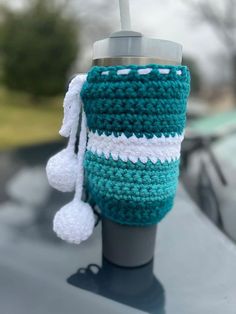 a crocheted cup cozying on top of a car with a tassel