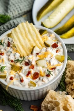 a white bowl filled with dip surrounded by crackers and pickle slices on the side