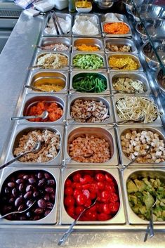 an assortment of different foods in trays lined up on a buffet table with utensils