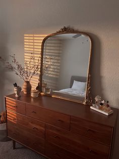 a dresser with a mirror and vases on top of it next to a bed