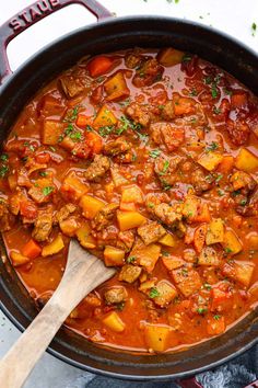 a large pot filled with stew next to a wooden spoon