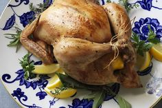 a whole chicken on a blue and white plate with lemons, parsley and herbs