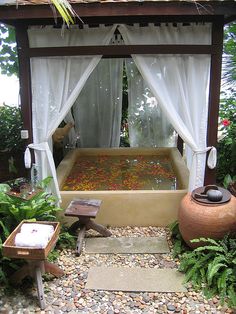 a gazebo in the middle of a garden filled with plants and flowers, next to an outdoor bathtub