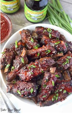 a plate full of ribs with sauce and green onions on the side next to two bottles of ketchup