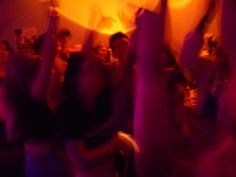 a group of people dancing in a room with lights on the ceiling and one person holding up his arms