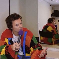 a man sitting in front of a mirror holding a microphone and wearing a colorful jacket