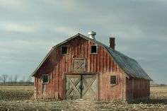 an old red barn sits in the middle of a large open field with no grass