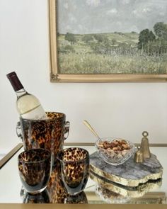 a glass table topped with leopard print cups and bowls filled with food next to a painting