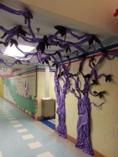 a hallway decorated with purple paper trees and bats hanging from the ceiling in an elementary school