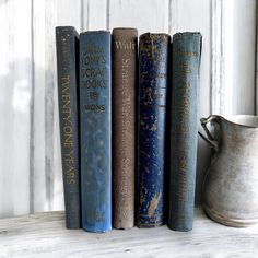 four books are lined up on a shelf next to a pitcher and vase with white paint