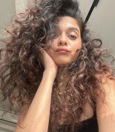 a woman with curly hair sitting in front of a mirror