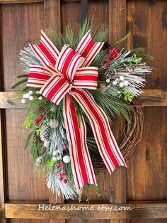 a christmas wreath with red and white striped bow hanging on a wooden door, surrounded by greenery