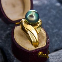 This timeless ring features a centered Tahitian pearl set above a swooping setting. The green overtones on the pearl contrast beautifully with the rich and hefty yellow gold mounting. The ring is crafted in 18k yellow gold and is currently a size 8. Classic Tahitian Pearl Ring For Formal Occasions, Yellow Gold Tahitian Pearl Ring Gift, Yellow Gold Tahitian Pearl Ring, Luxury Yellow Gold Tahitian Pearl Ring, Luxury Tahitian Pearl Ring In Yellow Gold, Wedding Tahitian Pearl Ring In Yellow Gold, Elegant Yellow Gold Tahitian Pearl Rings, Gift Yellow Gold Tahitian Pearl Ring, Gift Tahitian Pearl Ring In Yellow Gold