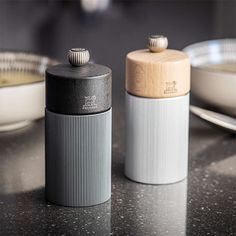 two salt and pepper shakers sitting on top of a counter next to a bowl