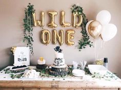 a table topped with cake and balloons in front of a wall that says wild one