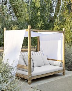 an outdoor day bed made out of wood and white fabric with pillows on it, in front of some trees