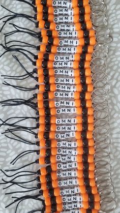 an orange and black beaded necklace is laying on a white tablecloth with silver beads