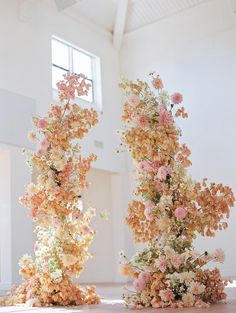 two tall vases filled with flowers on top of a wooden floor next to each other