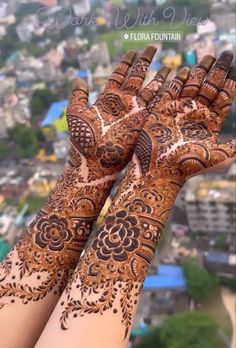 two hands with henna tattoos on them and the city in the backgroud