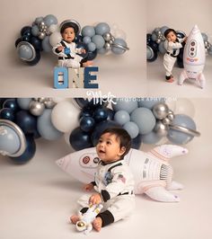 a baby in an astronaut suit sitting next to a rocket ship and balloon garlands