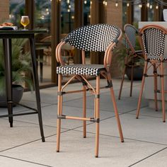 two wicker bar stools sitting next to each other on a patio with tables and chairs in the background