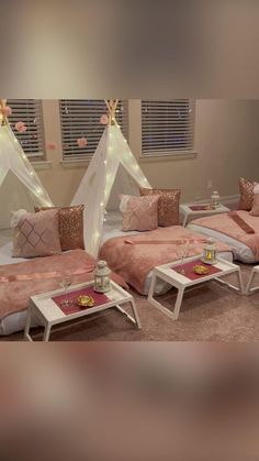 two beds with pink sheets and pillows are in a room that has lights on the windows