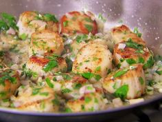 scallops and rice are being cooked in a pan on the stove with green garnish