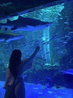 a woman standing in front of an aquarium looking at sharks