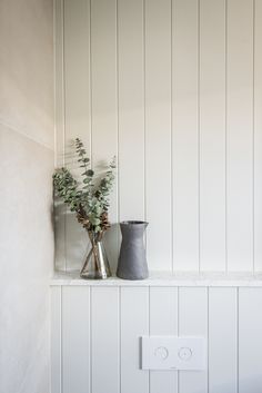 two vases with flowers are sitting on a shelf in the corner of a room