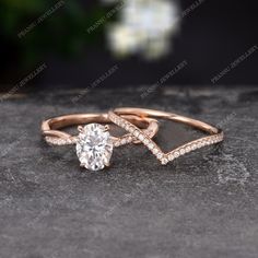 two gold rings with diamonds on them sitting on top of a stone surface in front of flowers