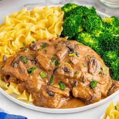 a white plate topped with pasta and meat covered in mushroom gravy next to broccoli