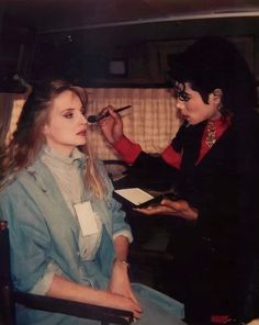 a woman is getting her makeup done while another person sits in a chair behind her