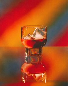 a glass filled with liquid sitting on top of a table next to a colorful wall