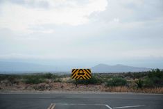 there is a yellow and black sign in the middle of the road with mountains in the background