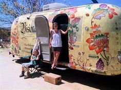 a woman is standing in the doorway of an old camper with flowers painted on it