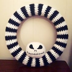 a crocheted jack skellingy pumpkin wreath on a wooden table next to a white wall