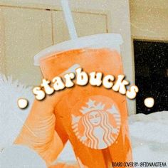 an orange starbucks cup sitting on top of snow covered ground