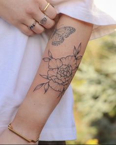 a woman's arm with a flower and butterfly tattoo on her left arm,